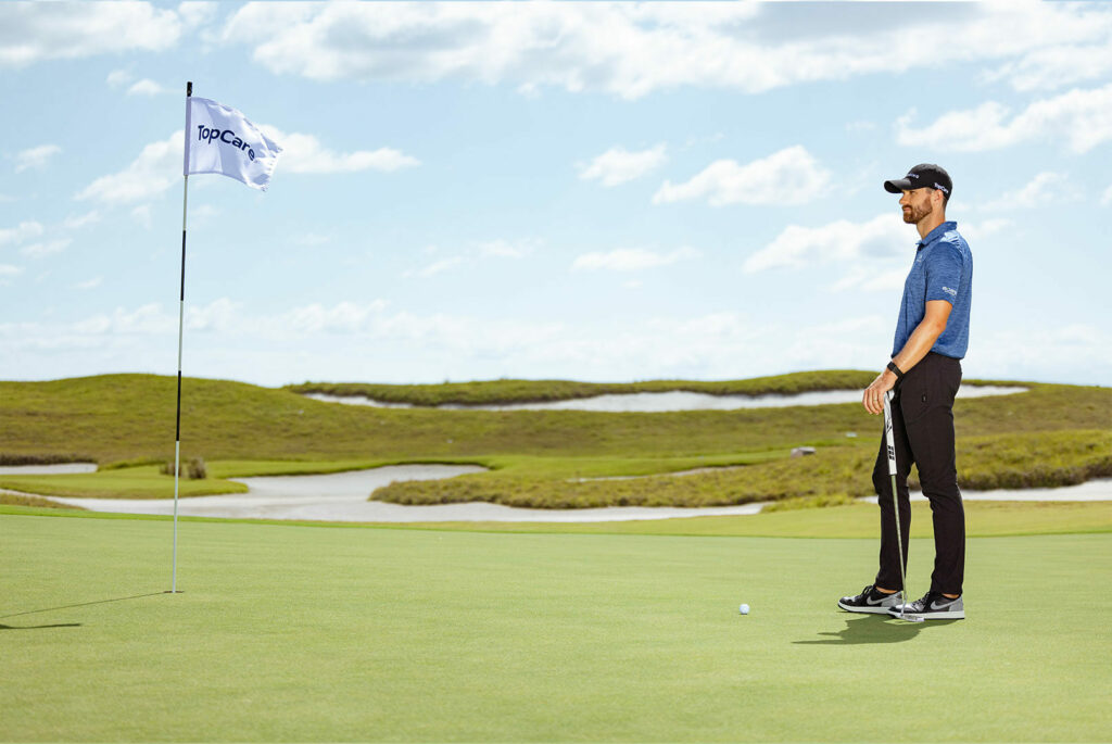 patrick rodgers on a golf course with a topcare flag